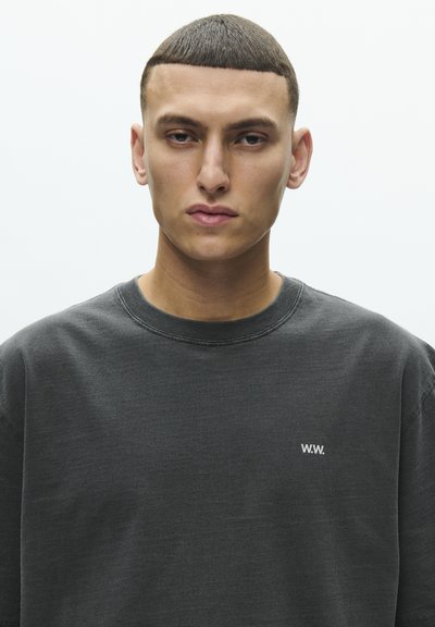 Mørkegrå genser laget av mykt stoff. Har rund hals og en liten hvit "W.W."-logo på venstre brystområde.