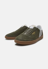 Zielone zamszowe trampki z białymi akcentami z siateczki, posiadające brązowe gumowe podeszwy i ukośne białe paski. Złoty detal z logo po boku.