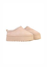 Beige ruskind slip-on sko med en kraftig sål, der har en tekstureret zigzagkant langs åbningen og en lille bagløkke for nem påtagning.