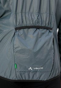Leichte, dunkelgraue Vaude-Jacke mit elastischem Bund und Rückentasche. Sie verfügt über einen glatten Stoff, kontrastierende schwarze Abschlüsse und ein Logodetail.