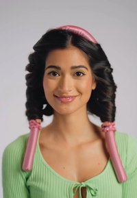 Modèle avec de longs cheveux bruns coiffés en grandes boucles, portant un haut côtelé vert menthe avec un nœud à l'avant ; cheveux ornés de bigoudis roses.