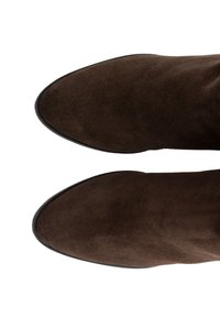 Bottines en daim marron avec un bout pointu, une semelle plate et une texture lisse. Le design présente des lignes épurées sans aucune pièce métallique apparente.