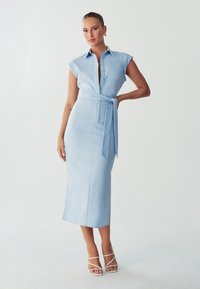 Hellblaues, ärmelloses Kleid mit Hemdkragen, durchgehender Knopfleiste, Taillenbund und seitlichem Schlitz. Glatte Stoffqualität mit figurbetonter Silhouette.