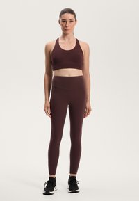 Den bordeauxfärgade träningssetet inkluderar en bralette och högmidjade leggings, båda med en jämn textur och en figurnära design. Bärs med svarta sneakers.