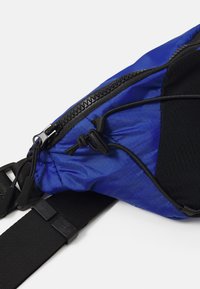 Blaue Stoff-Umhängetasche mit schwarzen Akzenten, ausgestattet mit einem Reißverschluss, einem verstellbaren Gurt und einer strukturierten Fläche. Leichtes und kompaktes Design.