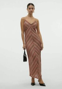 Vestido maxi com padrão de ziguezague em tons de vermelho e bege, com alças finas, uma silhueta ajustada e uma fenda lateral.