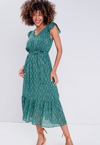 Green patterned maxi dress with a V-neck, ruffled sleeves, cinched waist, and tiered hemline. Made from lightweight fabric. Adjustable straps.