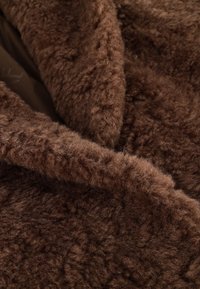 Bruine, donzige, getextureerde stof met een zachte glans, met een gelaagde uitstraling en subtiele golvenpatronen, geschikt voor buitenkleding of dekens.