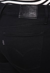 Jeans de mezclilla negra con una etiqueta de cuero de Levi's en la cintura, costuras en contraste y un diseño distintivo del bolsillo trasero en forma curva.