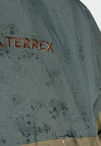 Water-resistant jacket featuring droplets on a dark gray fabric, with a light brown lower section and an embossed logo reading "WATERTEREX."