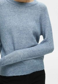 Vaaleansininen neulepaita, joka on valmistettu pehmeästä, teksturoidusta kankaasta. Siinä on pyöreä pääntie ja resorit hihansuissa. Hieman lyhennetty helma, jossa on hieman kuluneet reunat.