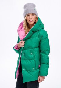 Zelená péřová bunda s růžovým podšíváním, velkou kapucí, drukovými knoflíky a prošívanou texturou. Spárováno se světle šedou čepicí.
