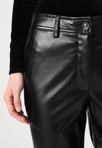 Pantalons en simili cuir noir avec une texture lisse, dotés d'une fermeture à bouton à l'avant, de passants de ceinture et de poches latérales.