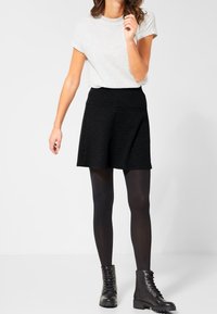 Falda skater negra de tejido texturizado, combinada con una camiseta de color gris claro y medias negras. Botas de tobillo negras con cordones completan el conjunto.