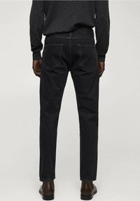 Jeans de mezclilla oscura con corte recto, que cuentan con bolsillos traseros y costuras en contraste. Llevados con un suéter gris ajustado y botas marrones.