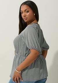 Blusa in gingham bianco e nero con maniche a palloncino corte, vita cincherata e vestibilità rilassata, realizzata in un tessuto leggero.