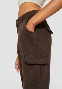 Bruine cargo broek met een textuurafwerking, voorzien van zijzakken, een knoopsluiting en een aansluitende taille.