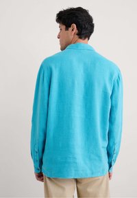 Camicia in lino turchese con vestibilità rilassata, maniche lunghe e polsini con bottoni. Presenta una texture morbida e un colletto.