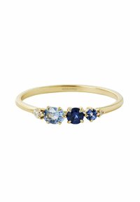 Anillo de oro que presenta tres piedras preciosas: azul pálido, azul profundo y azul oscuro, con un acento de piedra clara, mostrando una textura suave y un diseño sencillo.