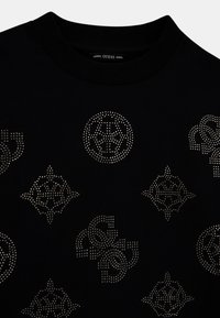 Mustan kankaan t-paita, jossa on hopeiset niittigeeniset kuviot ja logot. Pyöreä pääntie, jossa on ribbikuvio. Pehmeä rakenne.