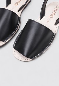 Sandalias de cuero negro que presentan un empeine ancho, punta abierta, costuras en los bordes y una plantilla de cuero natural.