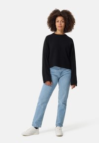 Un pull noir en tricot à la coupe décontractée, associé à un jean droit bleu clair et à des baskets blanches. Comprend des manches longues et un col rond.