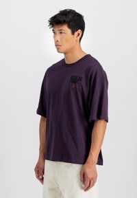 T-shirt oversized violet foncé en coton avec des manches courtes, présentant un logo BERLIN texturé en noir sur la poitrine gauche.