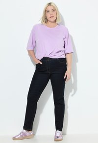 Světle fialové tričko s krátkým rukávem uvázané v pase, spárované s tmavými džíny a reflexními růžovými teniskami na bílém pozadí.