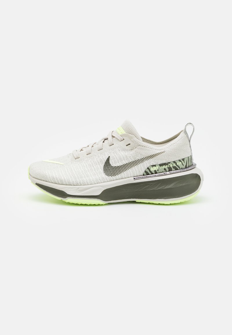 Gaišgrey skriešanas apavi ar teksturētu virsu, melnais Nike swoosh, atstarojoši akcenti un mīksta zole ar zaļu ārējo daļu.