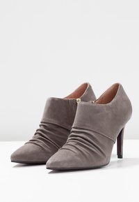 Grå mocka högklackade stövletter med spetsig tå, samlad textur överframme, och en diskret guldfärgad dragkedja bak.