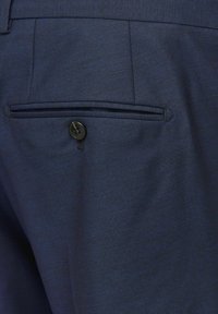 Un pantalon bleu marine présente un tissu texturé, une poche arrière unique avec une fermeture à bouton noir et une coupe élégante et ajustée.