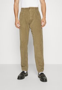Pantaloni in corduroy verde oliva con design a gamba dritta, dotati di chiusura con bottone, tessuto testurizzato e tasche frontali. Mocassini neri sotto.