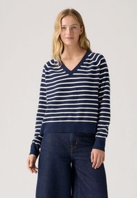 Jersey a rayas azul marino y blanco con cuello en V, mangas largas y dobladillo cropped. Tejido suave con puños y cinturilla acanalados.