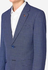 Sakó s vzorom houndstooth v modrej a čiernej farbe, s jedným gombíkom, klopovými goliermi a oranžovým akcentom na ľavom golieri.