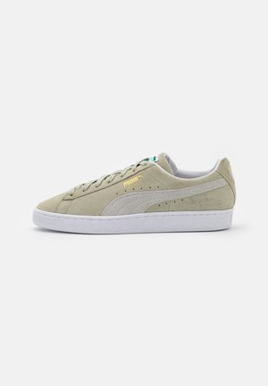 Jasnozielony zamszowy sneaker marki Puma z białą podeszwą, sznurowadłami i paskiem Puma po boku, widoczny z lewego profilu na białym tle.