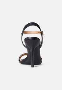 Sandalo con tacco alto nero dal design elegante, caratterizzato da uno schienale curvo, una sottile cinghia attorno alla caviglia e una finitura lucida.