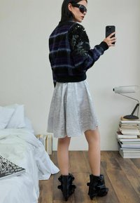 Czarna i fioletowa kurtka bomberka w kratę z teksturowanymi kwiatowymi zdobieniami, zestawiona ze srebrną plisowaną spódnicą i czarnymi botkami z falbankami przy kostce.