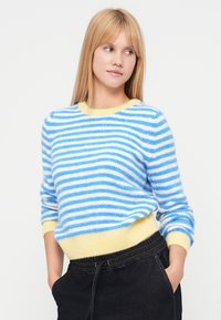 Modro-bel pulover z mehko teksturo, z rumenim ovratnikom in spodnjim robom. Rokavi so dolgi in rahlo ohlapni.