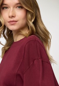 Felpa bordeaux con scollo rotondo e vestibilità comoda. Tessuto morbido con dettagli di cuciture visibili e spalle leggermente scese.