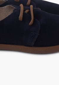 Scarpe in suede blu navy con lacci marroni, punta tonda, superficie testurizzata e suola in gomma marrone. Presentano dettagli cuciti.