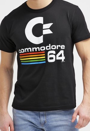 Zwart katoenen T-shirt met een groot wit "C"-logo, het woord "Commodore" en regenboogstrepen boven het nummer "64." Standaard pasvorm.
