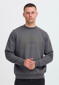 Sweatshirt gris en mélange de coton, avec des poignets et un col côtelés. Graphique sur le devant en texte jaune indiquant "Mélange de qualité supérieure 1993."
