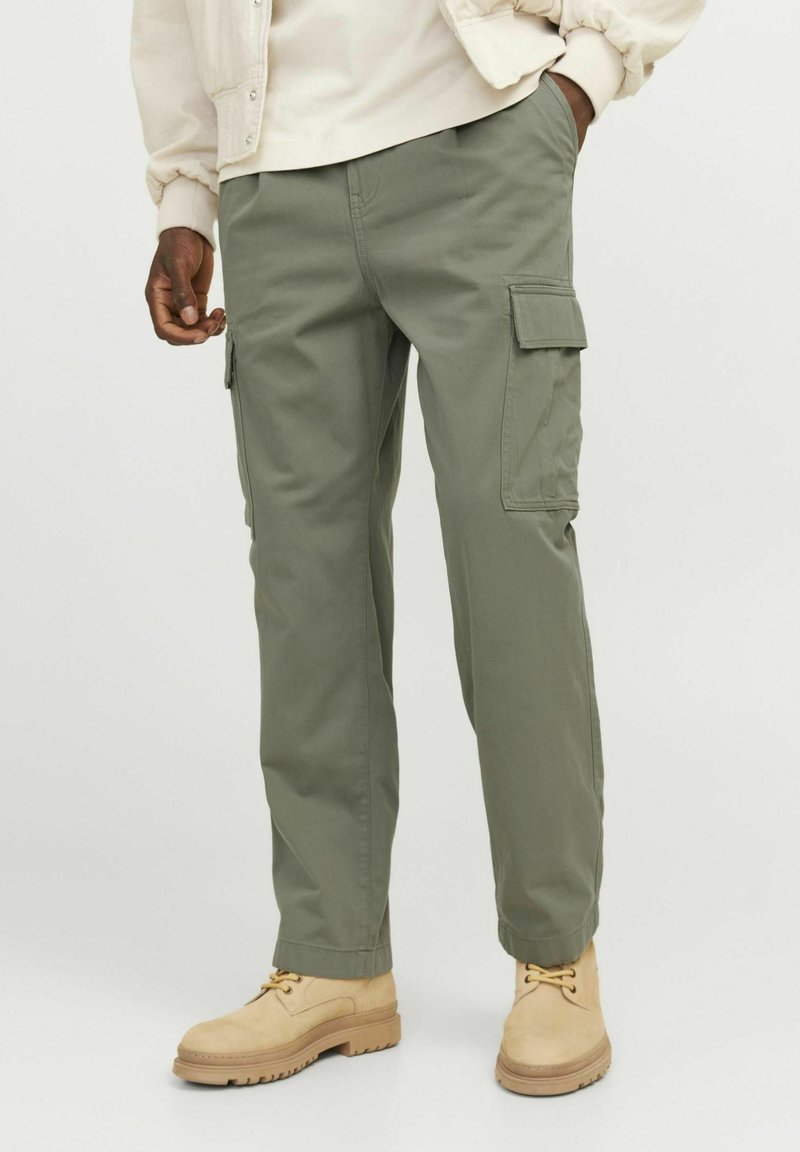 Cargo pants in light olive green fabric, featuring side pockets, straight cut, and worn with tan boots. Smooth texture, casual design.