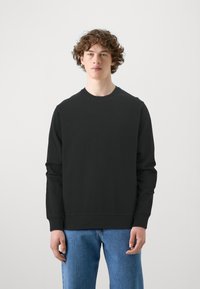 Sort crewneck sweatshirt i bomuld med lange ærmer. Har et minimalistisk design, almindelig pasform og ribbede manchetter. Båret sammen med blå denim jeans.
