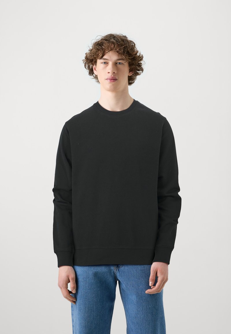 Sort crewneck sweatshirt i bomuld med lange ærmer. Har et minimalistisk design, almindelig pasform og ribbede manchetter. Båret sammen med blå denim jeans.