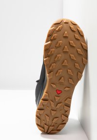 Suela de zapato de senderismo negra con un patrón de superficie de goma robusto. Presenta un acento rojo y una suela naranja texturizada para mayor agarre en diversas superficies.