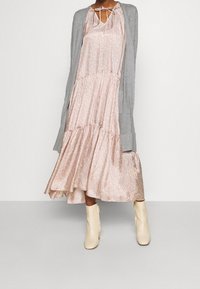 Rosa Blumenmusterkleid mit einem gestuften Design, kombiniert mit einer hellgrauen Strickjacke und cremefarbenen Knöchelschuhen. Glattes Material mit einem leichten Glanz.