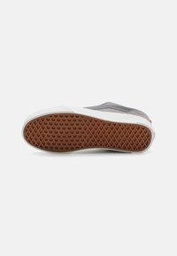 But z gumową podeszwą z teksturowanym wzorem w jodełkę, szarym wierzchem i białym noskiem o gładkim wykończeniu.