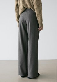 Pantalon gris à fines rayures, coupe large, associé à un pull beige texturé. Tissu lisse et coupe ajustée à la taille.