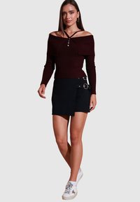 Burgundi off-shoulder dryžuotas marškinėlis su mygtukų detale, derinamas su juoda apvyniota sijonu, kurio šonuose yra kišenės ir metalinės detalės. Baltos sportbačiai.